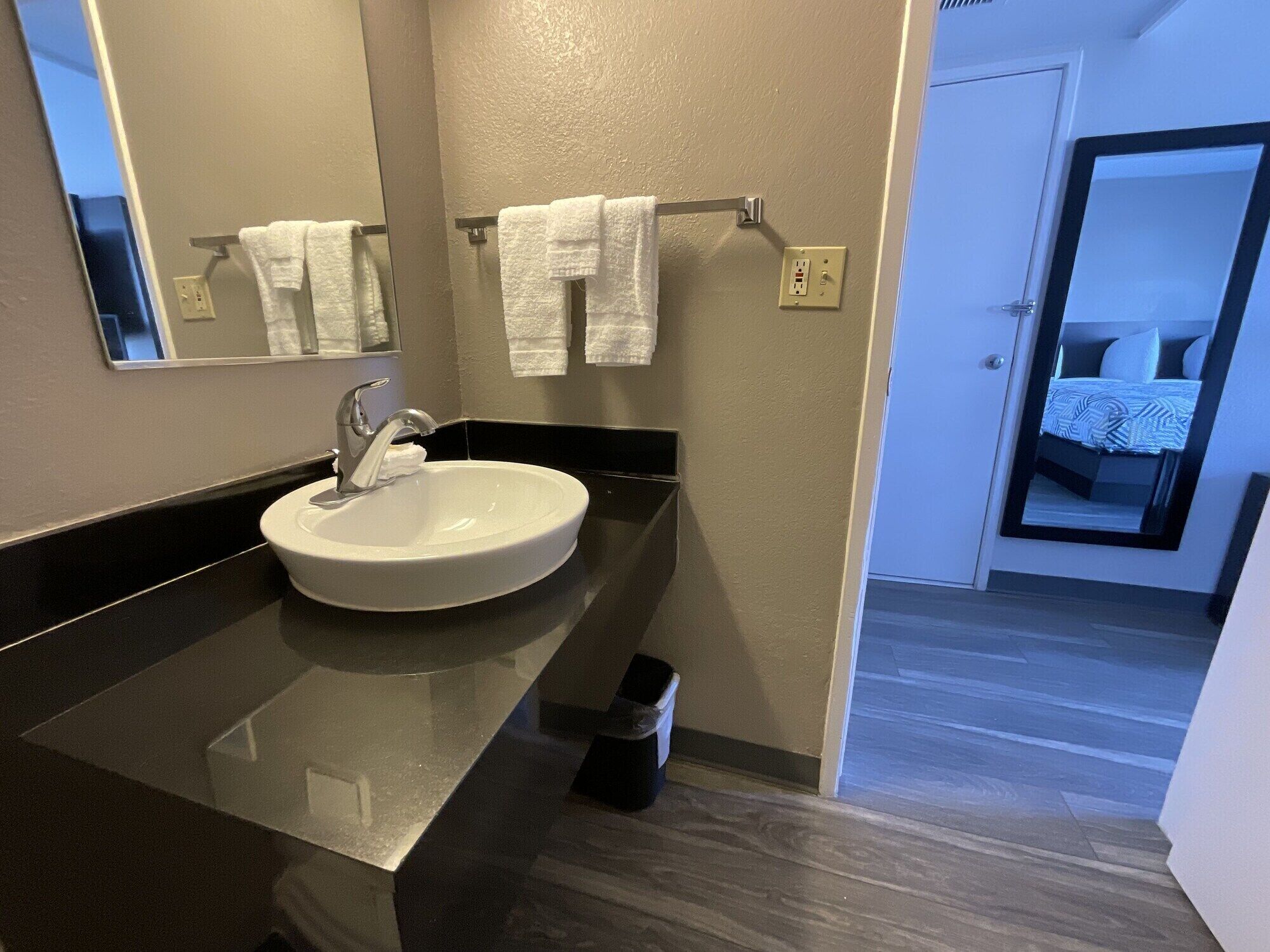 A modern bathroom with a white sink, black countertop, and a mirror above it. There are two white towels hanging on a rack.