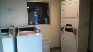 A laundry room with commercial washers and dryers, a window, and a trash can. - Motel 6 Ely, NV (Ely)