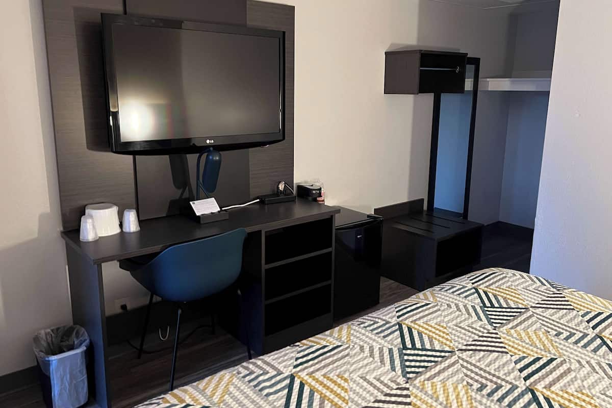 Habitación de hotel con cama, escritorio con computadora, televisor y basurero.