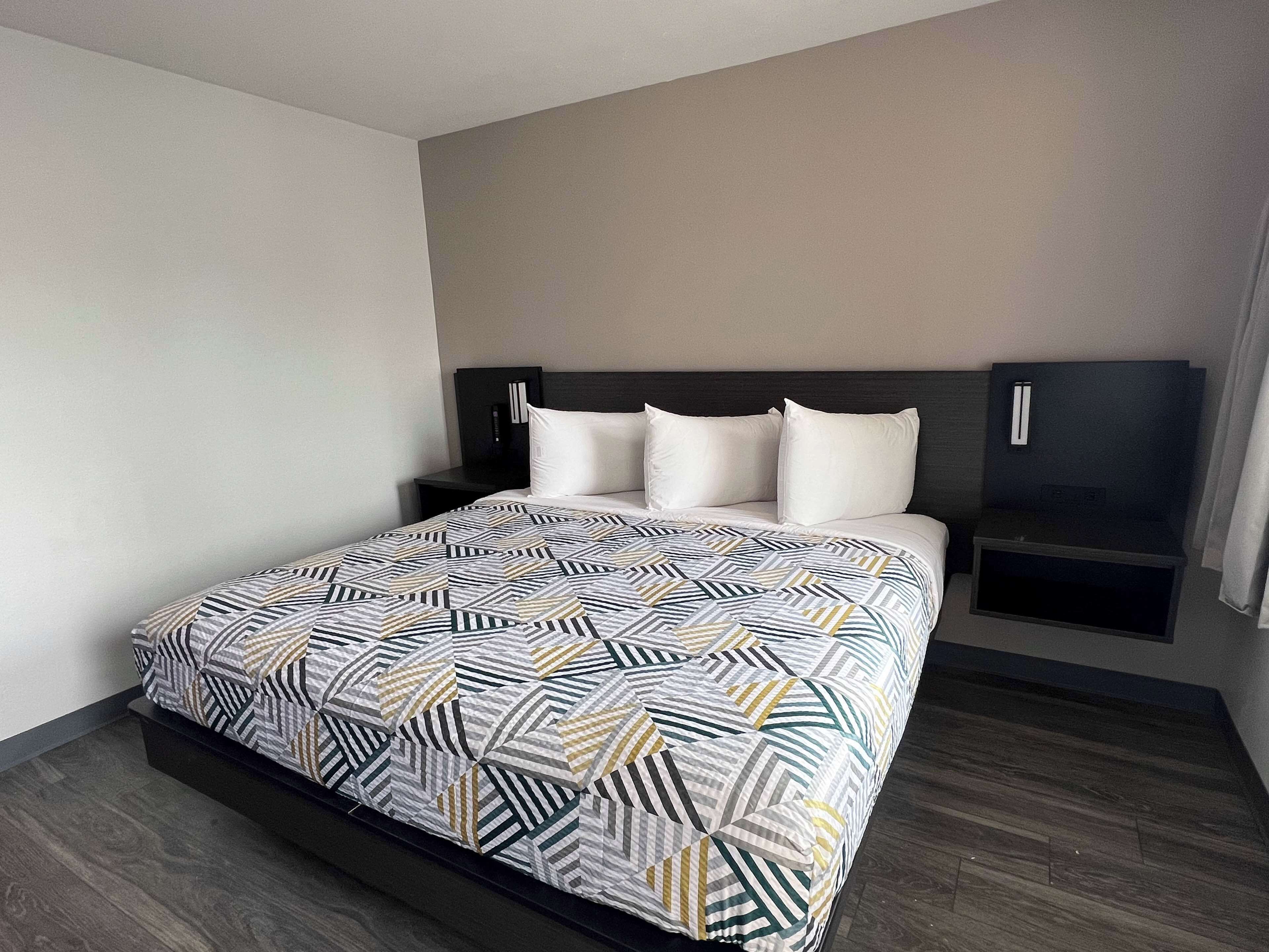 Een moderne hotelkamer met een groot bed, een donker hoofdeinde en een ingebouwde televisie aan de muur.