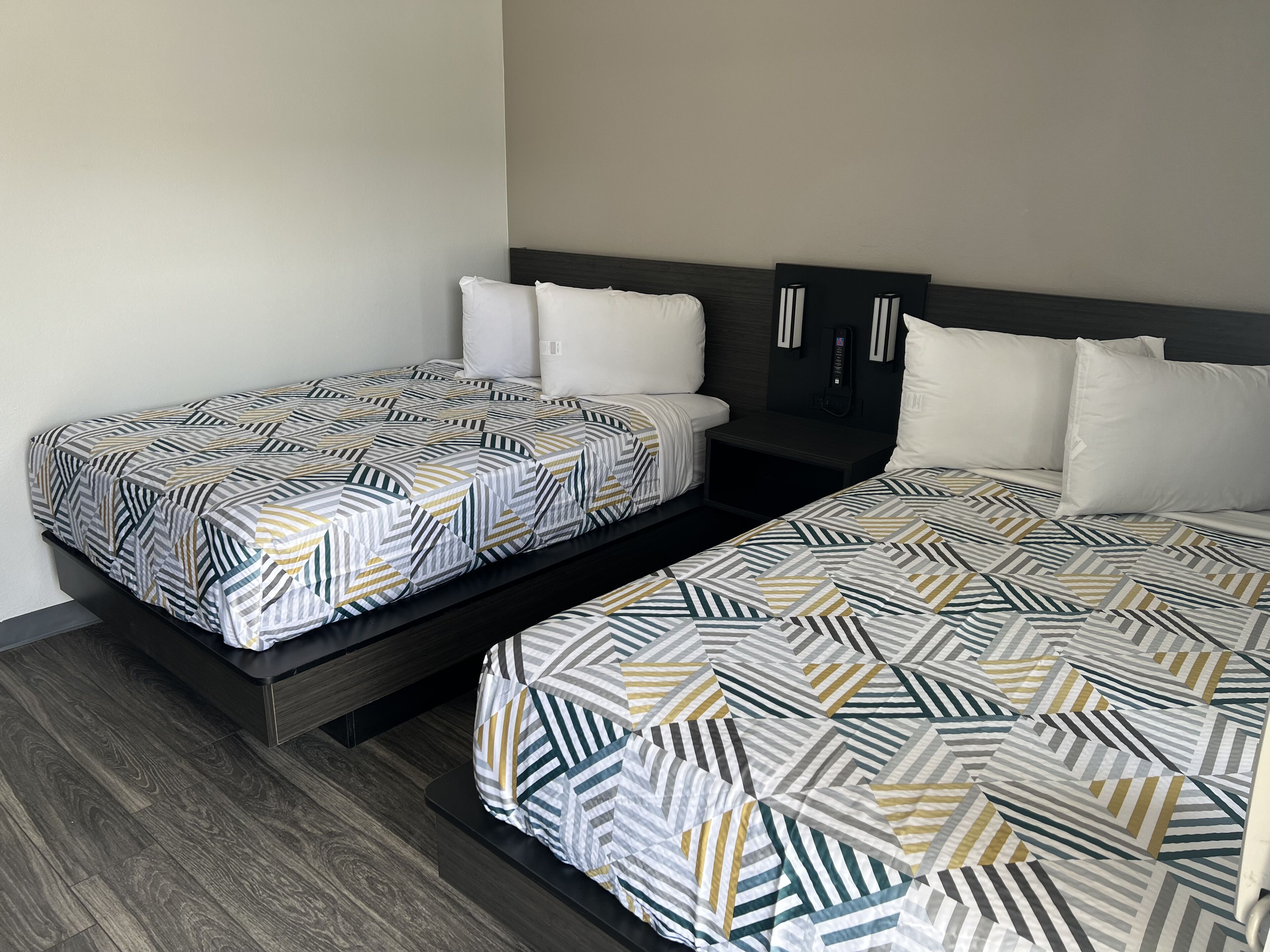 Two single beds with geometric patterned bedding, a dark headboard, and a bedside table with a phone.