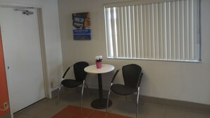 A small room with two black chairs around a white table, a poster on the wall, a window with blinds, and a door. - Motel 6 Ely, NV (Ely)