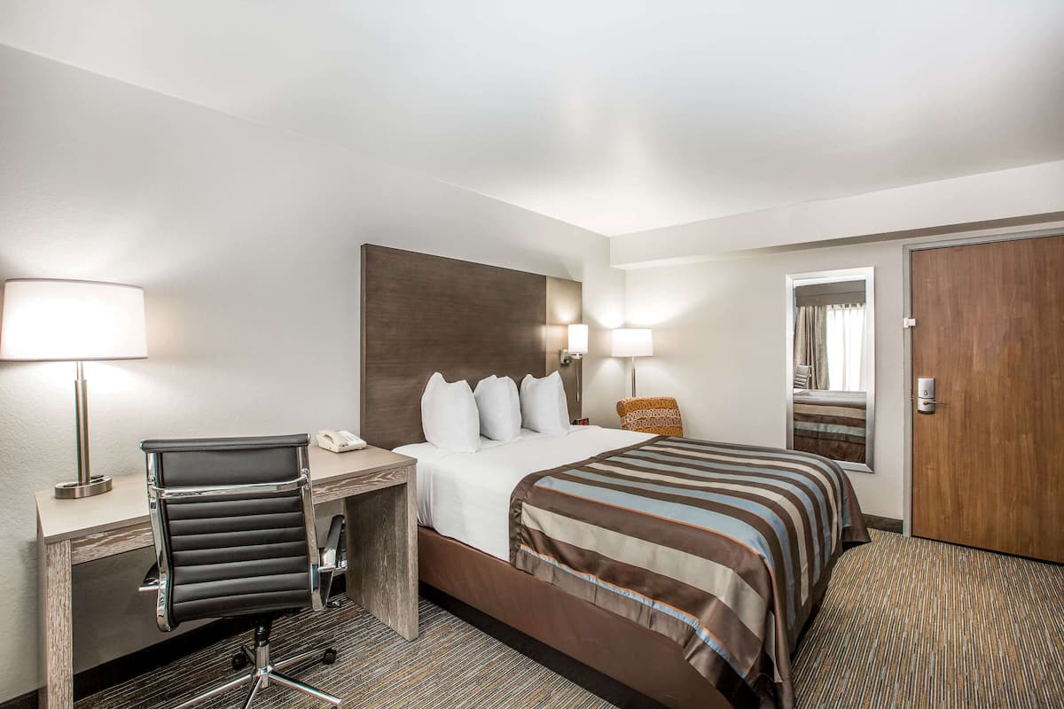 A hotel room with a bed, desk, chair, and a door.