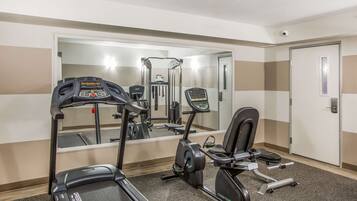 A gym with a treadmill, elliptical, and weight machine, a mirror, and a door.