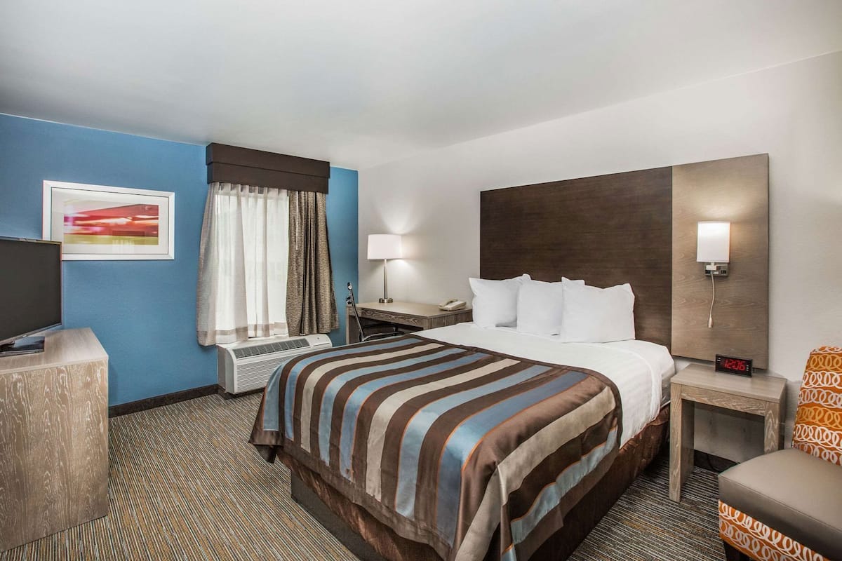 A hotel room with a bed, bedside table, lamp, TV, and a painting on the wall.