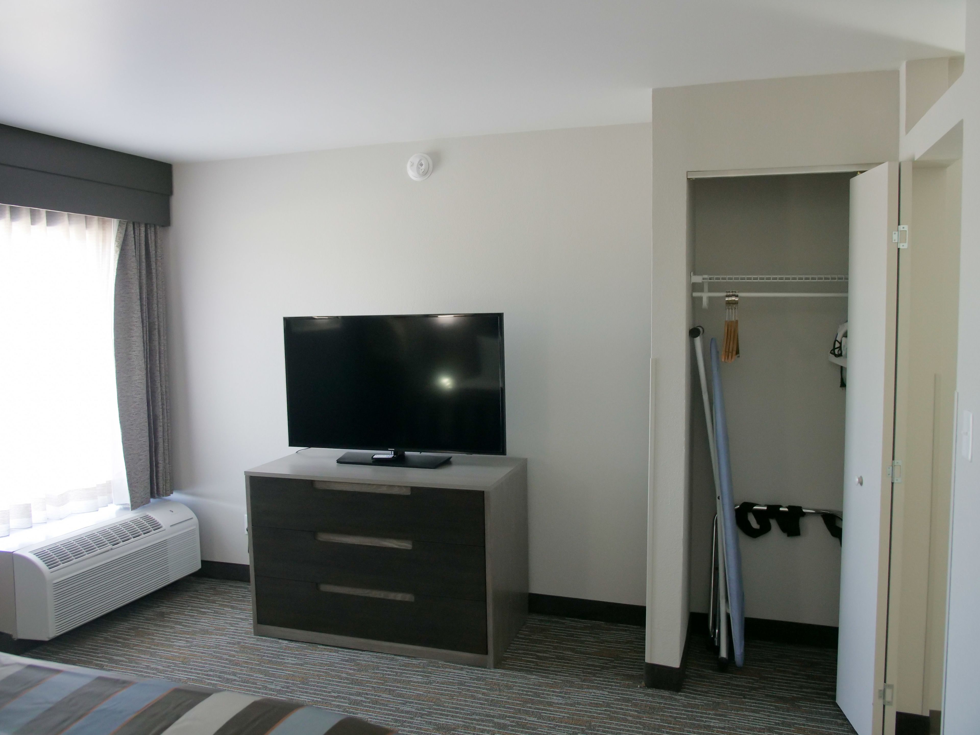 Habitación de hotel con televisor de pantalla plana en una cómoda, armario de acceso directo y ventana con cortinas.