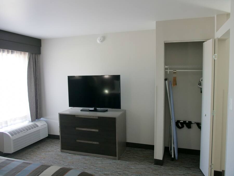 Habitación de hotel con televisor de pantalla plana en una cómoda, armario de acceso directo y ventana con cortinas.