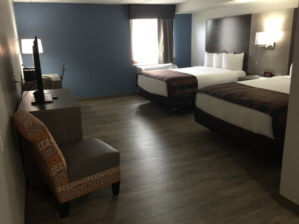 A hotel room with two beds, a desk, a chair, and a window with curtains.