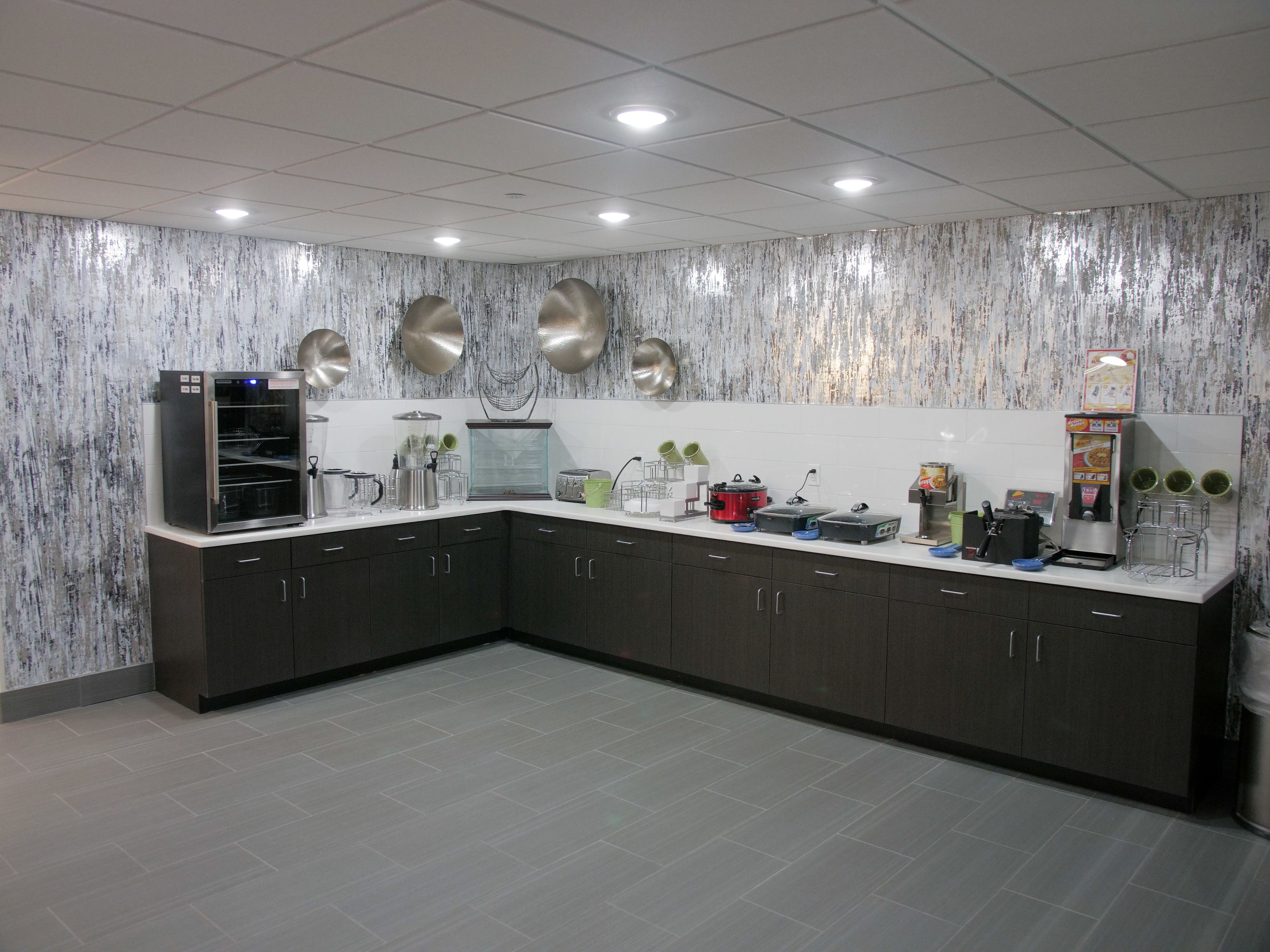 A modern kitchen with dark cabinets, a stainless steel refrigerator, a coffee machine, and a microwave.
