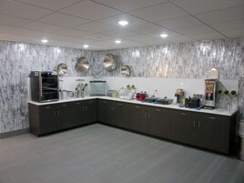 A modern kitchen with dark cabinets, a stainless steel refrigerator, a coffee machine, and a microwave.