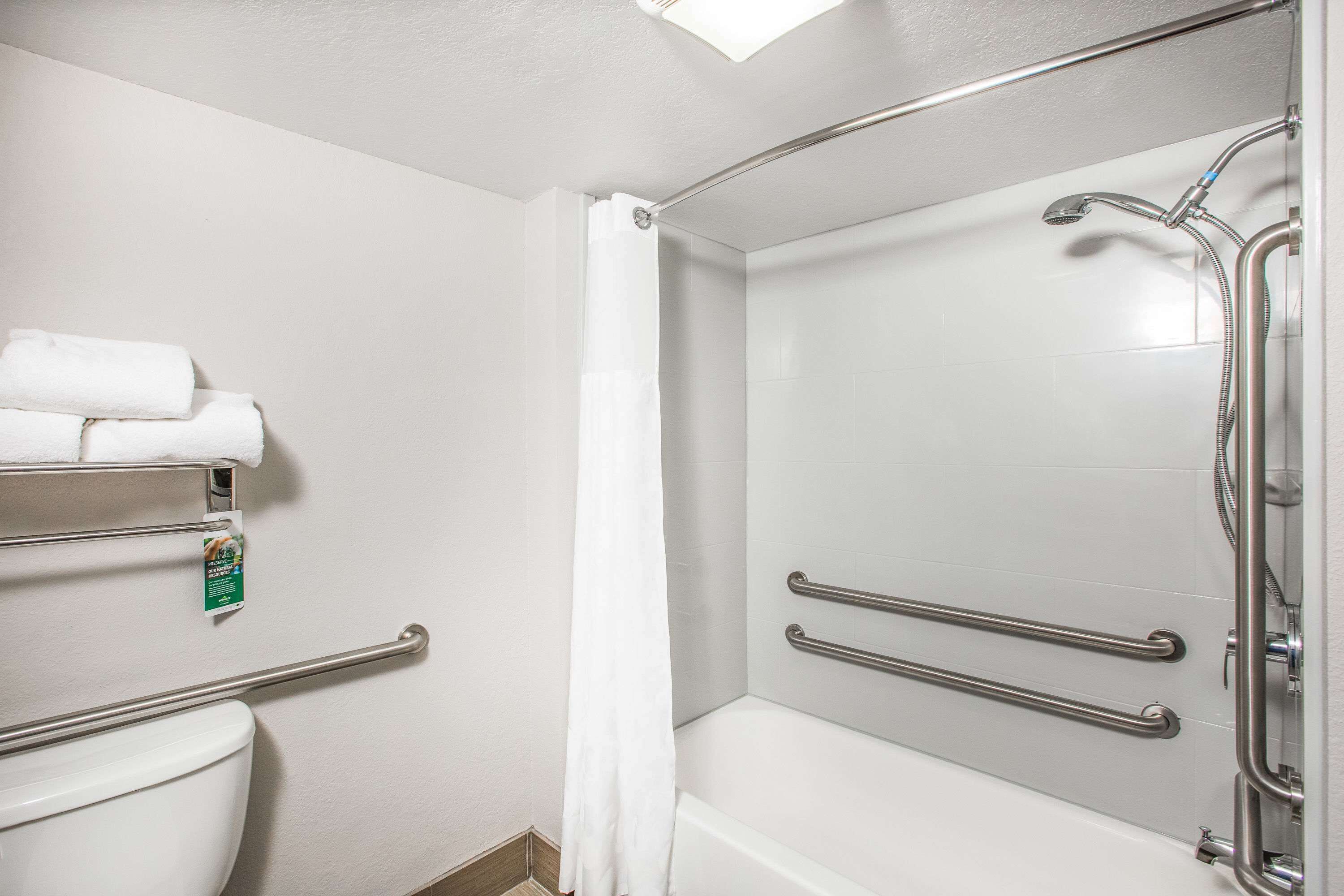 Un baño con inodoro, ducha con barras de apoyo y un perchero para toallas.