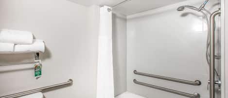 A bathroom with a toilet, a shower with grab bars, and a towel rack.