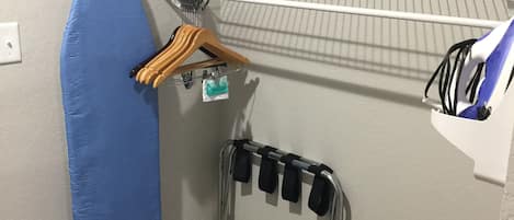 A corner of a room with a blue exercise mat, a metal rack with hangers, and a white shelf with a whiteboard.