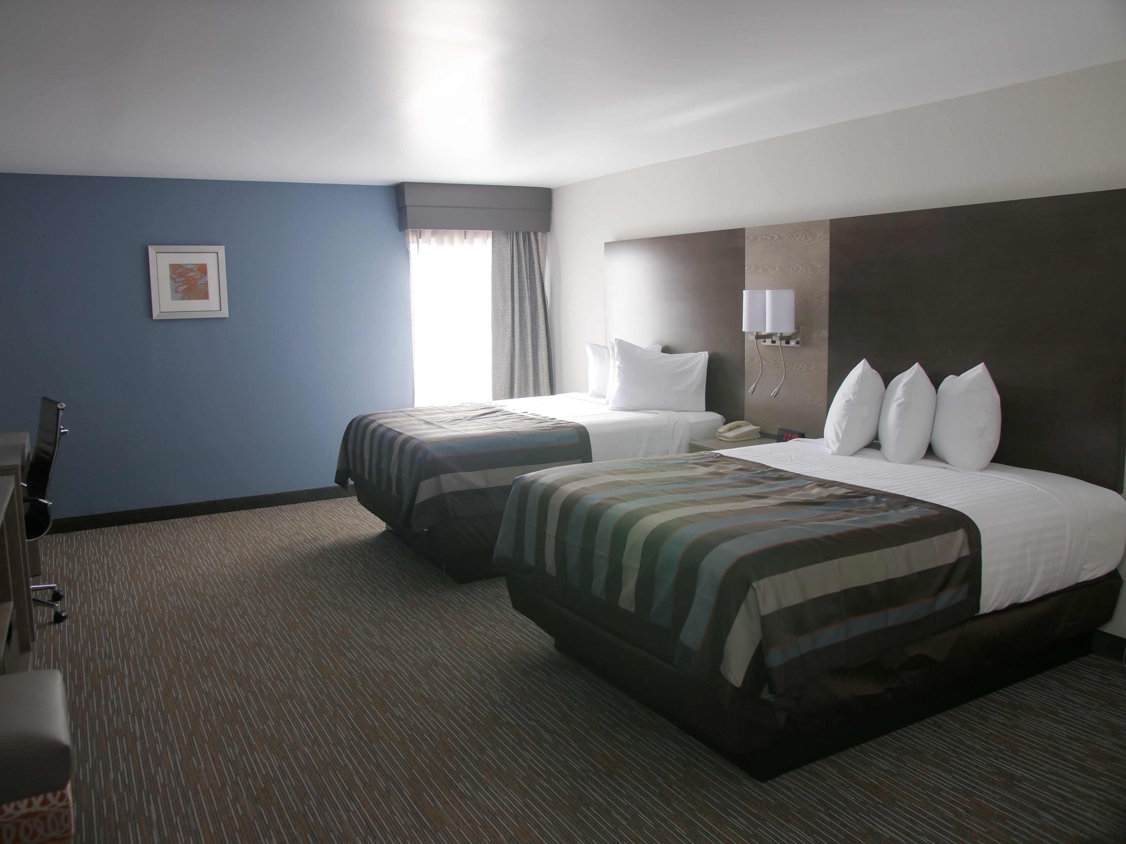 Habitación de hotel con dos camas, un escritorio, una silla y una ventana con cortinas.