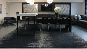 Un interior moderno con una mesa isla central, sillas negras, un sofá y un televisor de pantalla plana en la pared.