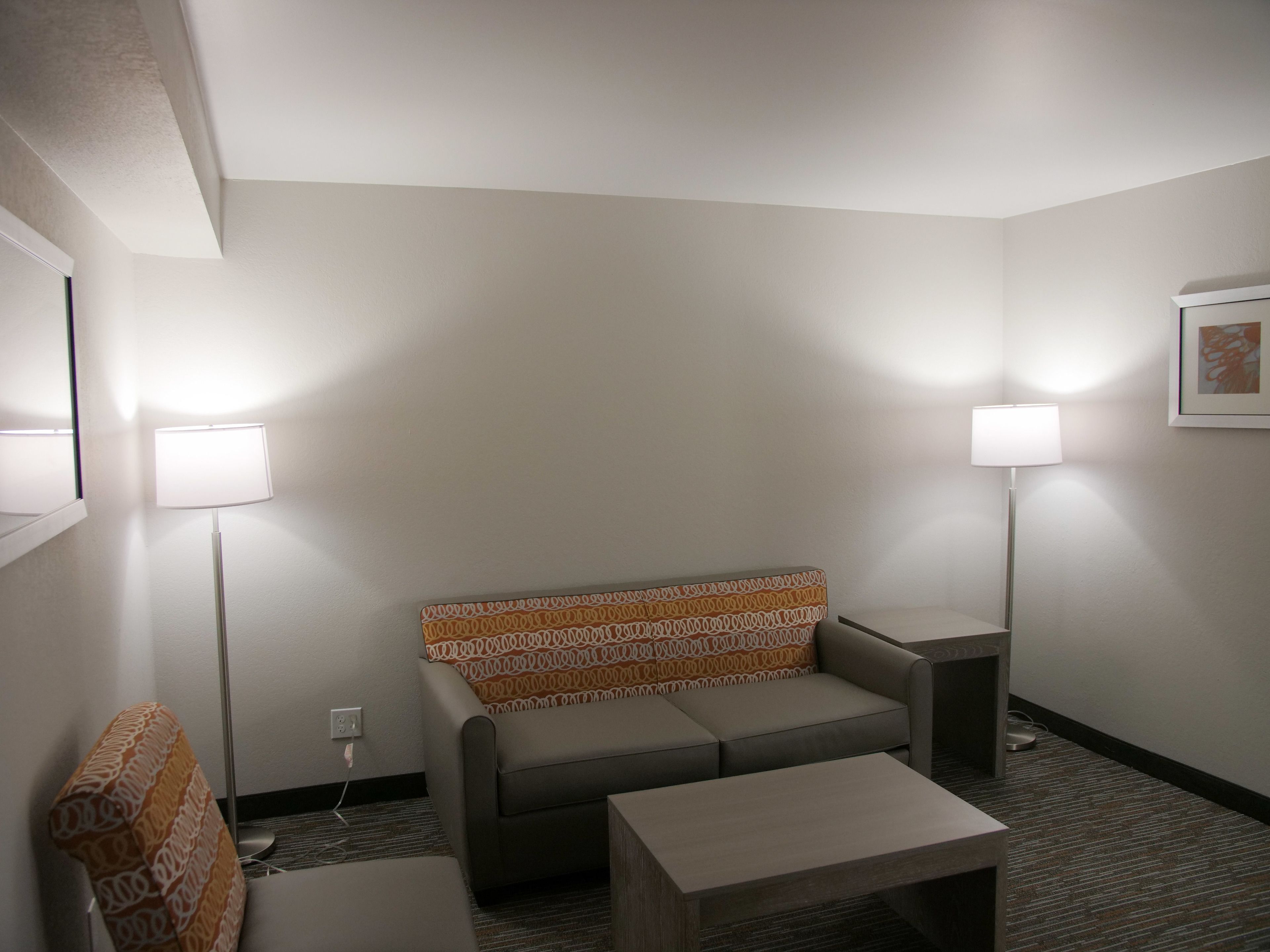 Una habitación de hotel con un sofá, una mesita y dos lámparas de pie.