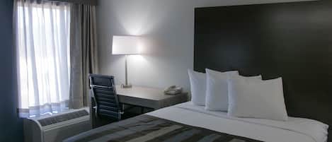 A hotel room with a bed, a desk, a chair, a lamp, and a telephone.