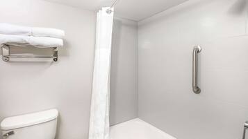 Un baño con inodoro, ducha con barra de apoyo y toallero con toallas.