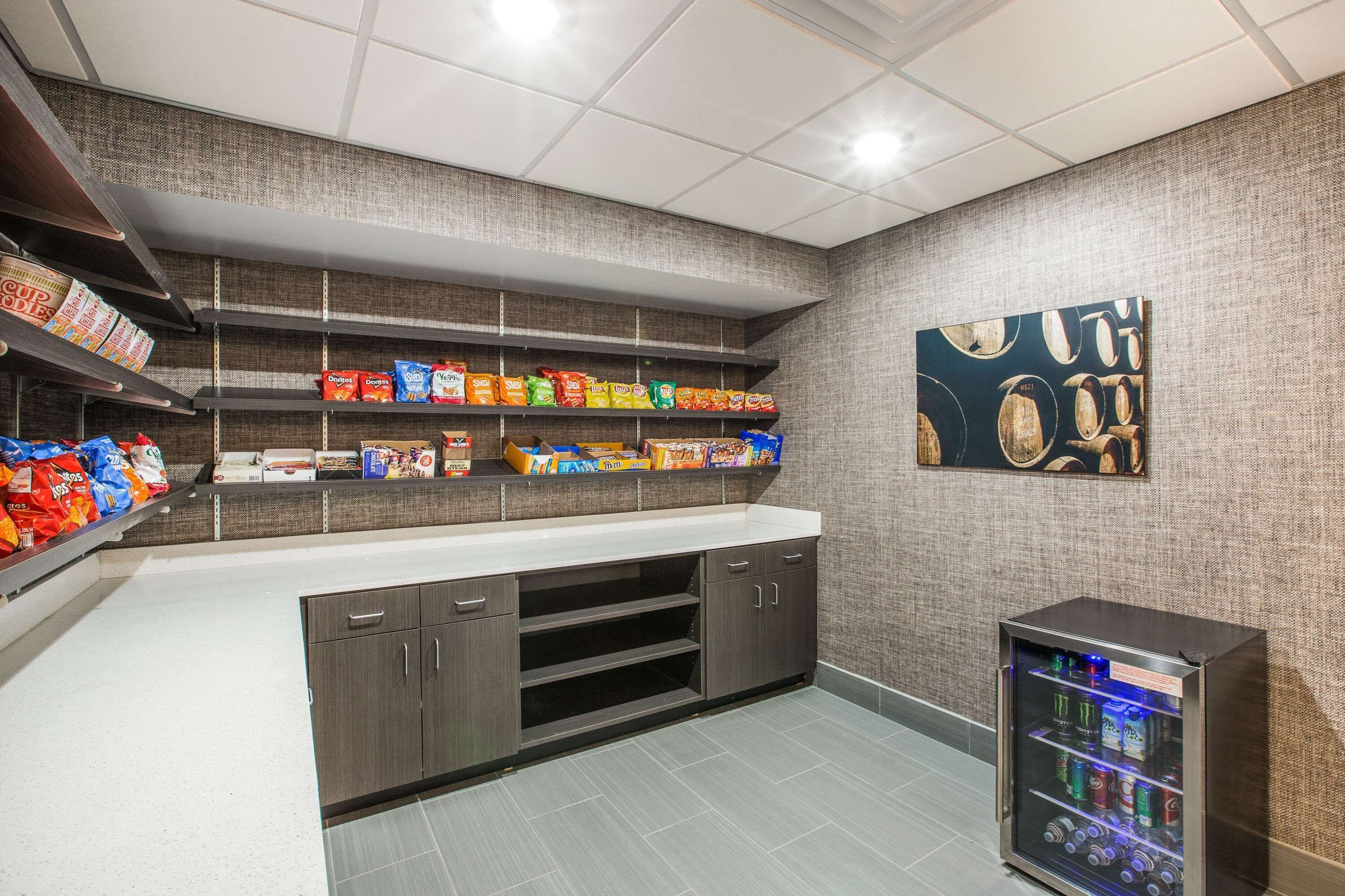 A kitchenette with shelves stocked with snacks, a refrigerator, and a painting on the wall.