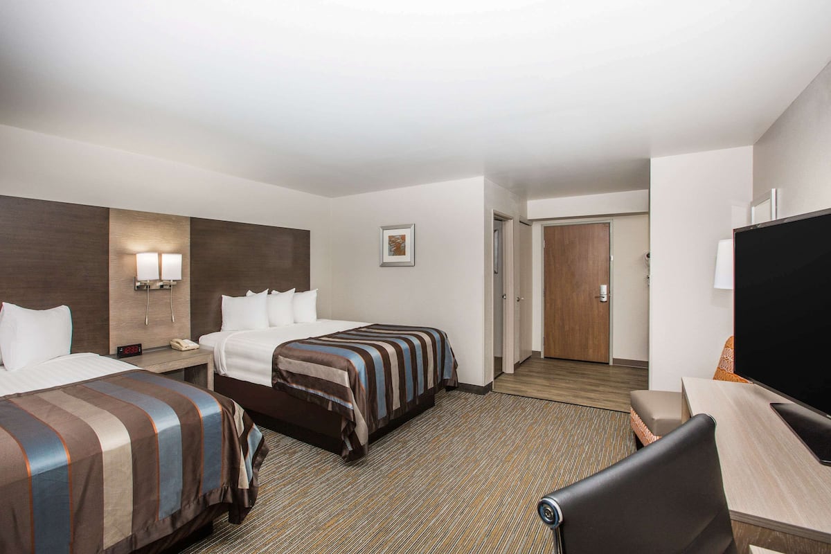 A hotel room with two beds, a desk, a television, and a door leading to another room.