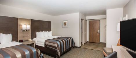 Habitación de hotel con dos camas, un escritorio, un televisor y una puerta que da a otra habitación.