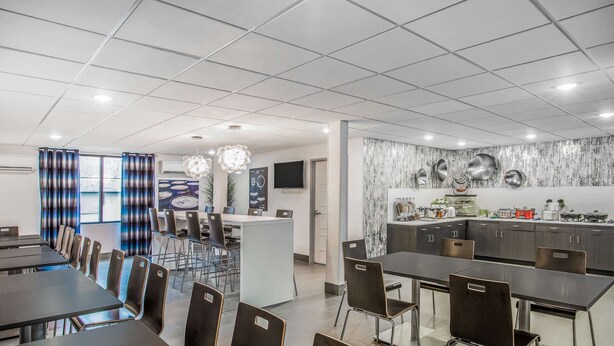 Un comedor moderno con varias mesas y sillas, una zona de cocina con electrodomésticos de acero inoxidable y un amplio ventanal con cortinas azules.