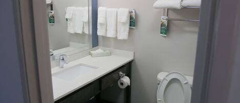 A compact hotel bathroom with a white sink, a mirror, a toilet, and a towel rack with folded towels.