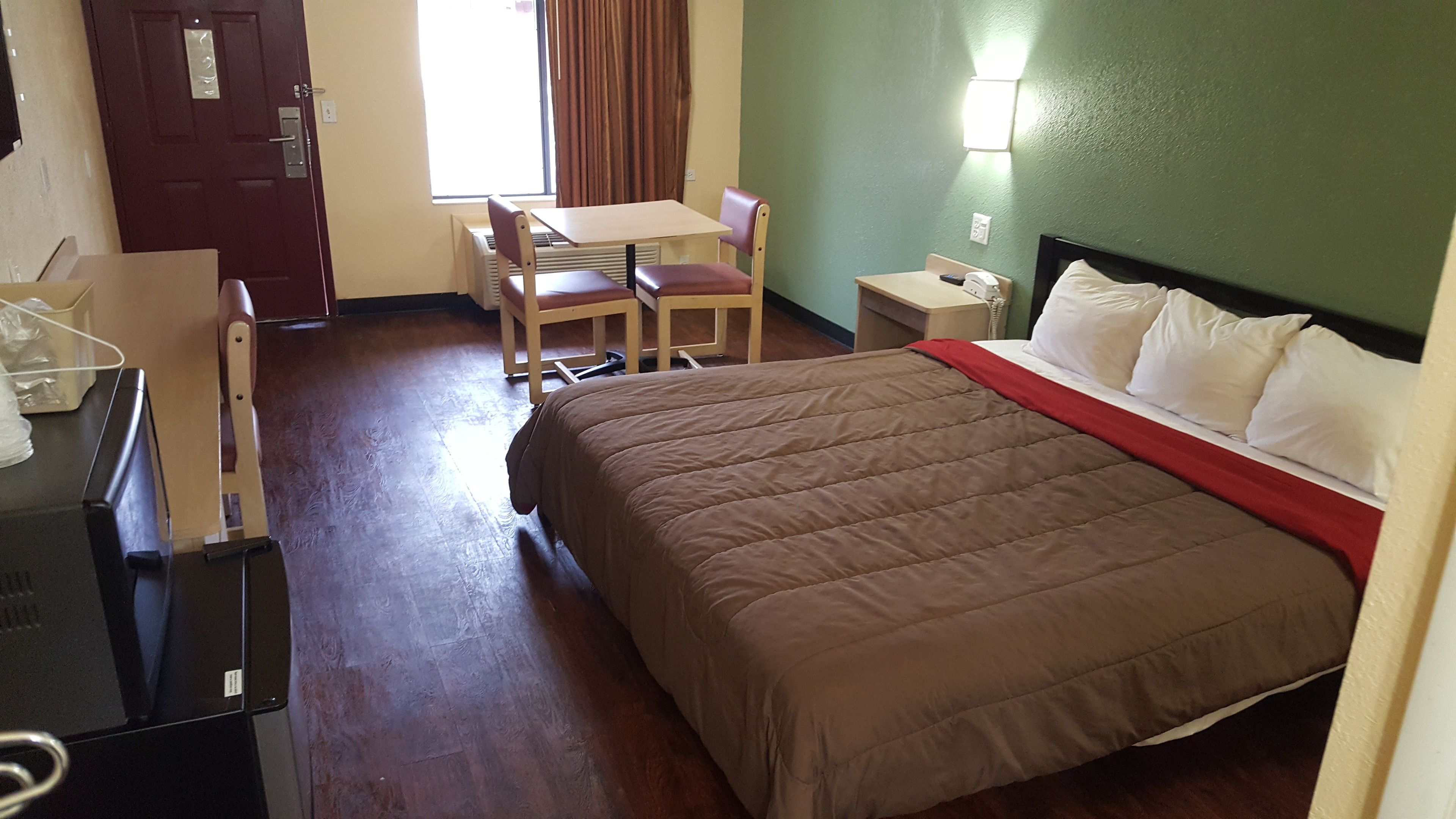 A hotel room with a bed, a desk, a chair, a telephone, and a window with curtains.