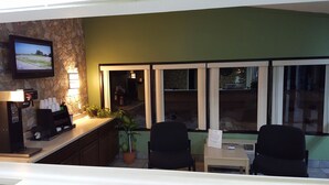 Un área de recepción con pared de piedra, televisor montado, cafetera y dos sillas frente a una ventana.