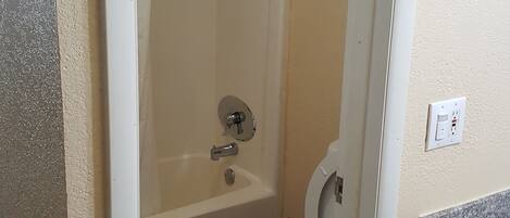 A bathroom with a bathtub, toilet, and a trash bin.