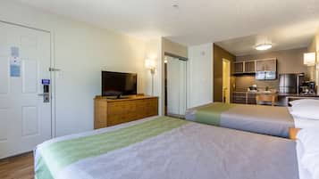 Habitación de hotel con dos camas, un televisor en una cómoda, una kitchenette y una puerta con un cartel.