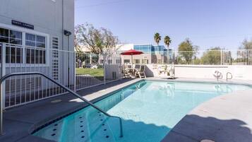 A swimming pool with a metal ladder, a red umbrella, and a sign for guest laundry.