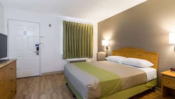 A hotel room with a bed, a desk, a television, a window with curtains, and a wall-mounted lamp.