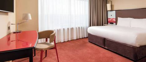 Une chambre d’hôtel avec un lit, un bureau, une chaise et une grande fenêtre avec des rideaux.