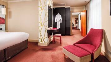 Una habitación de hotel con una cama, un sillón rojo, una mesita, un televisor y un armario.