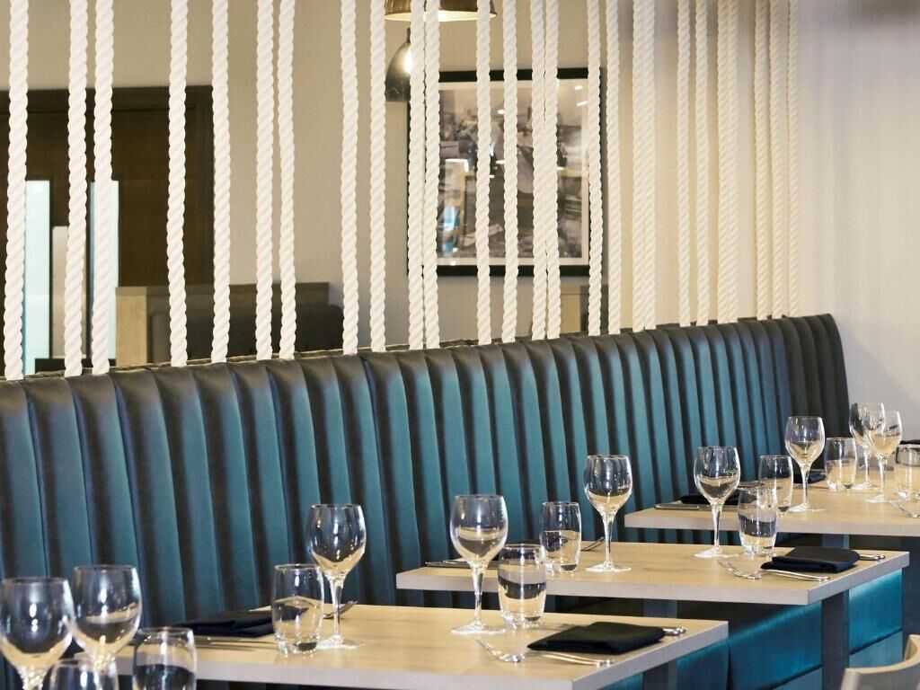 A restaurant interior with a row of booths and tables, each with a set of wine glasses and cutlery.