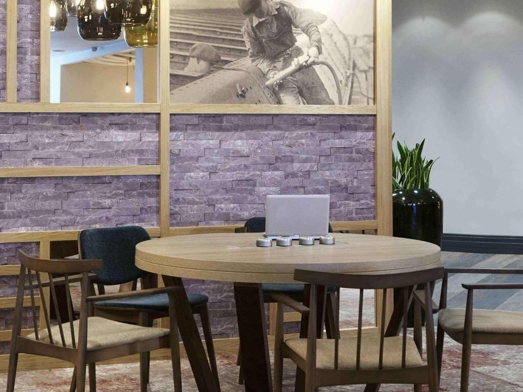 A round wooden table with four chairs, a laptop, and a small plant on the table.