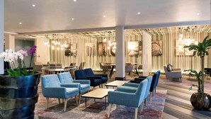 A modern lounge area with sofas, tables, and potted plants.