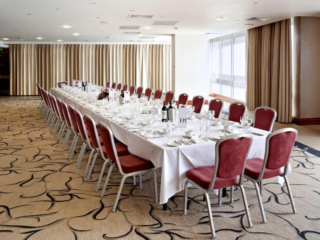 A conference room with a long table set for a meeting, red chairs, and a carpeted floor.