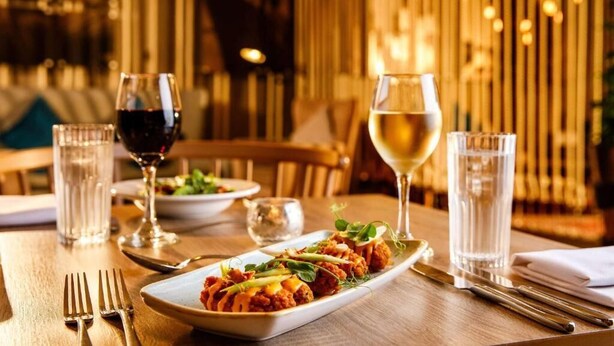 A dining table with a plate of food, two glasses of wine, and cutlery.