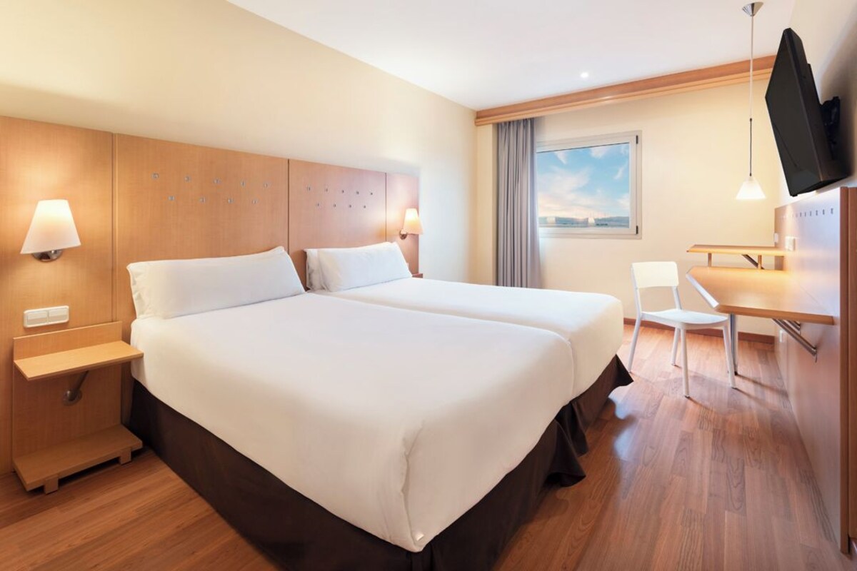 A hotel room with two beds, a desk, a chair, a TV, and a window with a view.