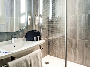 Un baño con un lavamanos blanco, un espejo, una toalla y una zona de ducha.
