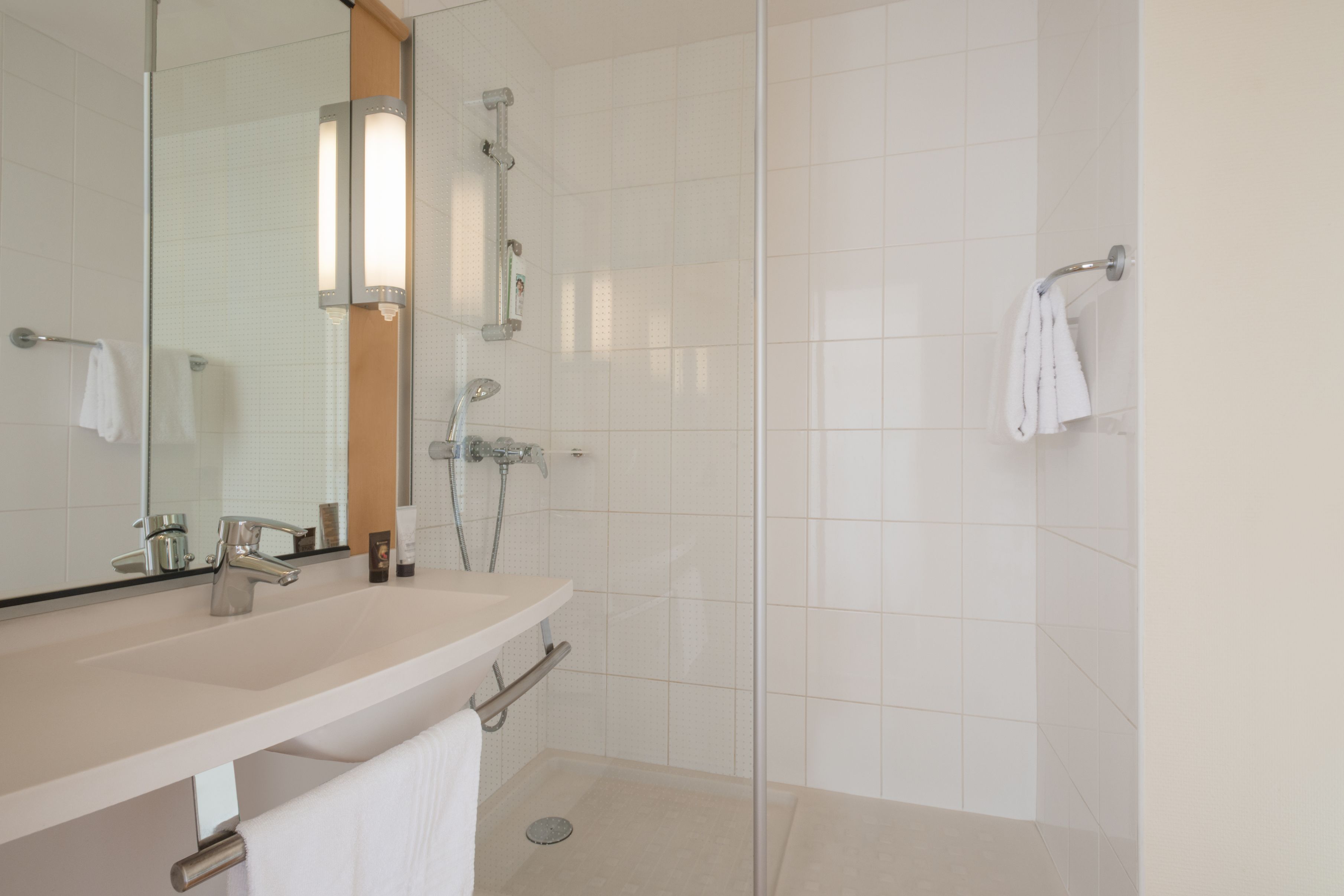 A modern bathroom with a large mirror, a sink, a shower, and a toilet.