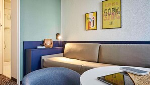 Une chambre d’hôtel moderne avec un canapé, une table ronde et deux œuvres d’art murales.