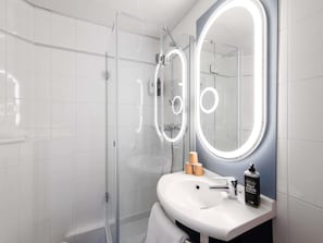 A modern bathroom with a glass shower enclosure, a white sink with a mirror, and a soap dispenser. - ibis Paris Avenue d'Italie 13ème (Paris)