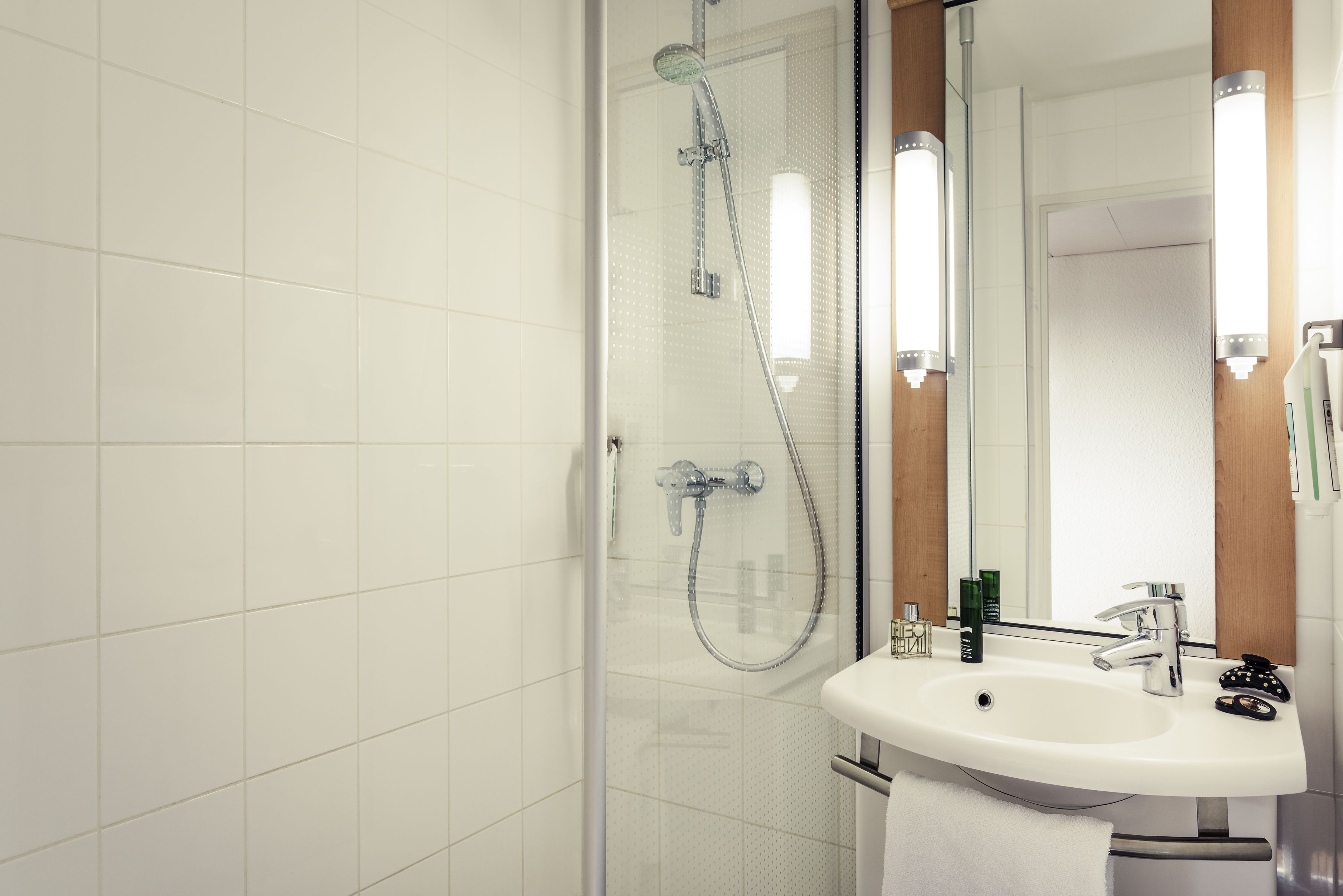 Een moderne badkamer met een glazen douchecabine, een witte wastafel en een spiegel met verlichting.