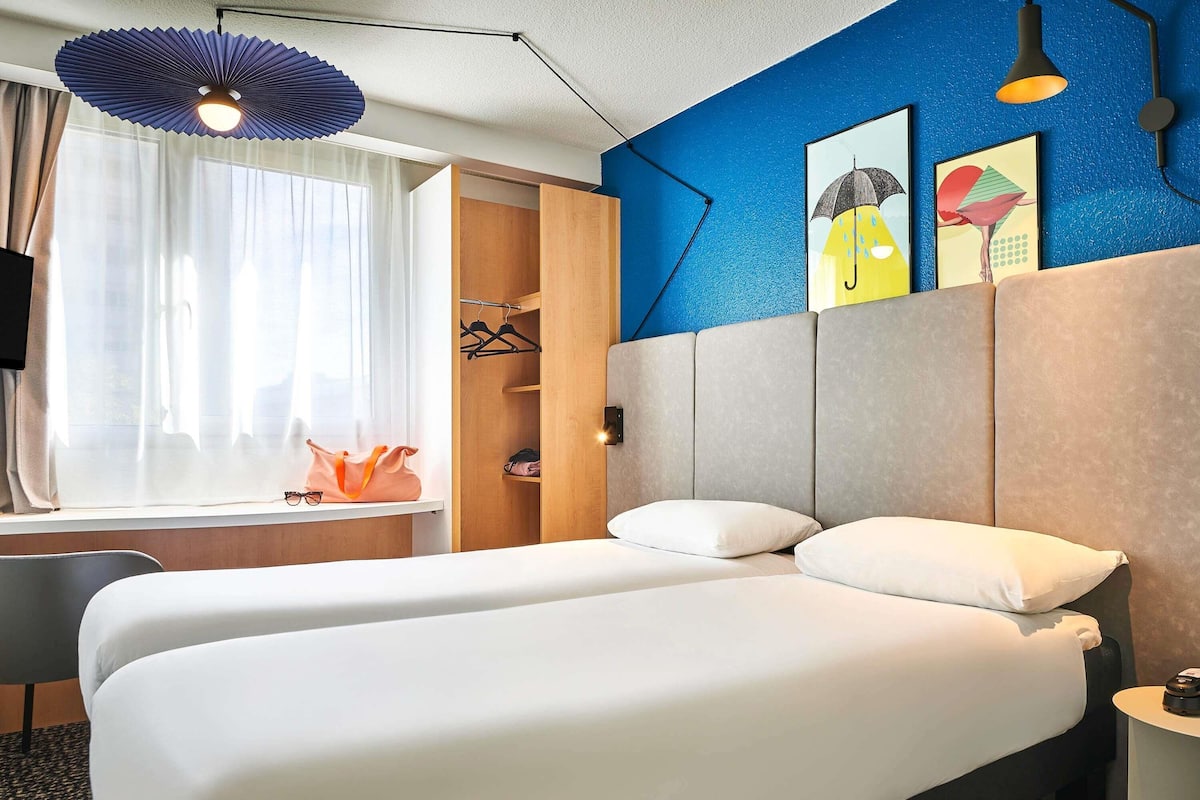 Habitación de hotel con dos camas, un armario, un escritorio y una ventana con cortinas.