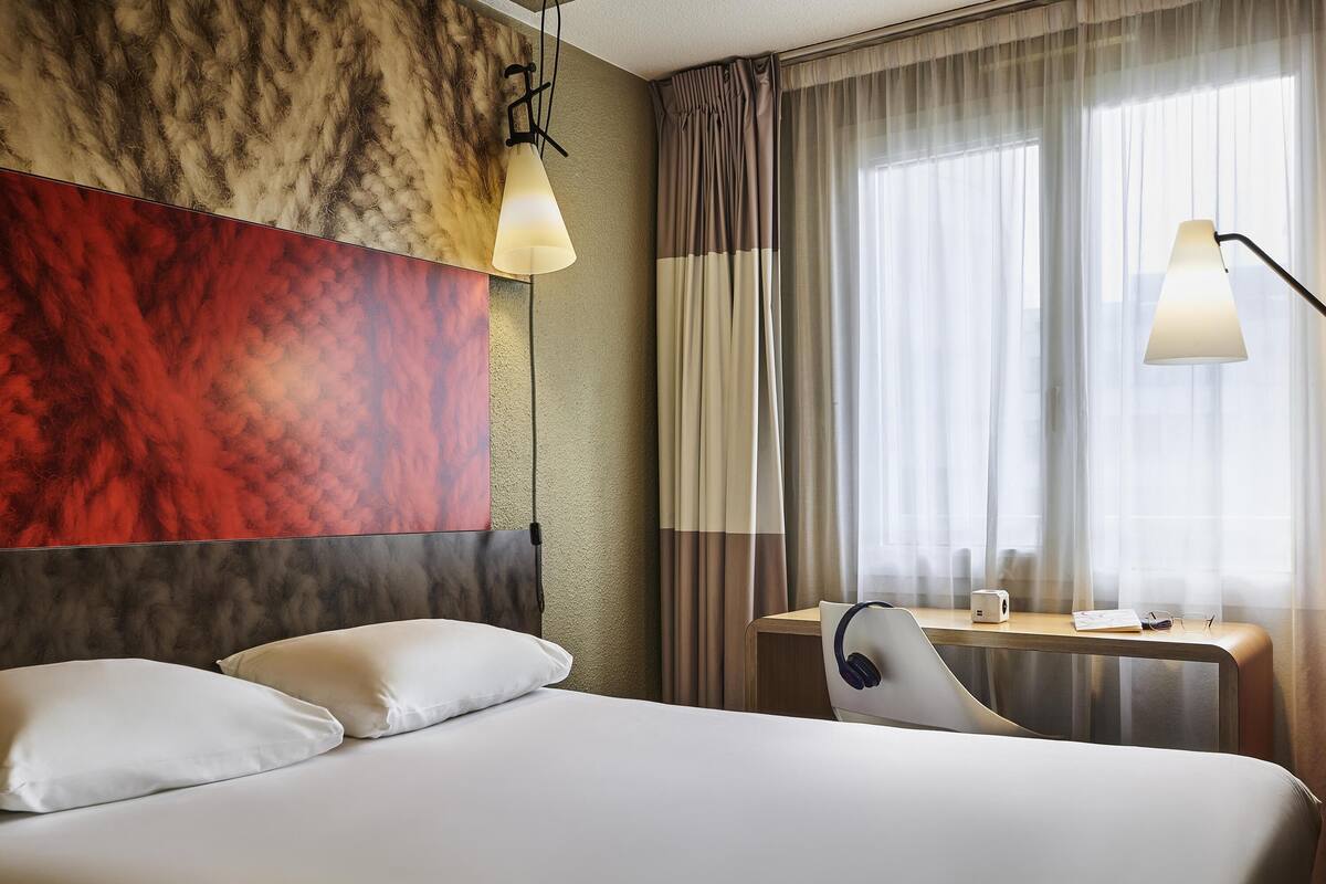 Una habitación de hotel con una cama, un escritorio con una computadora portátil y una ventana con cortinas.