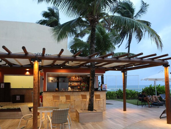 An outdoor bar area with seating, a pool, and a view of the ocean. - Mercure Salvador Rio Vermelho Hotel (Salvador)