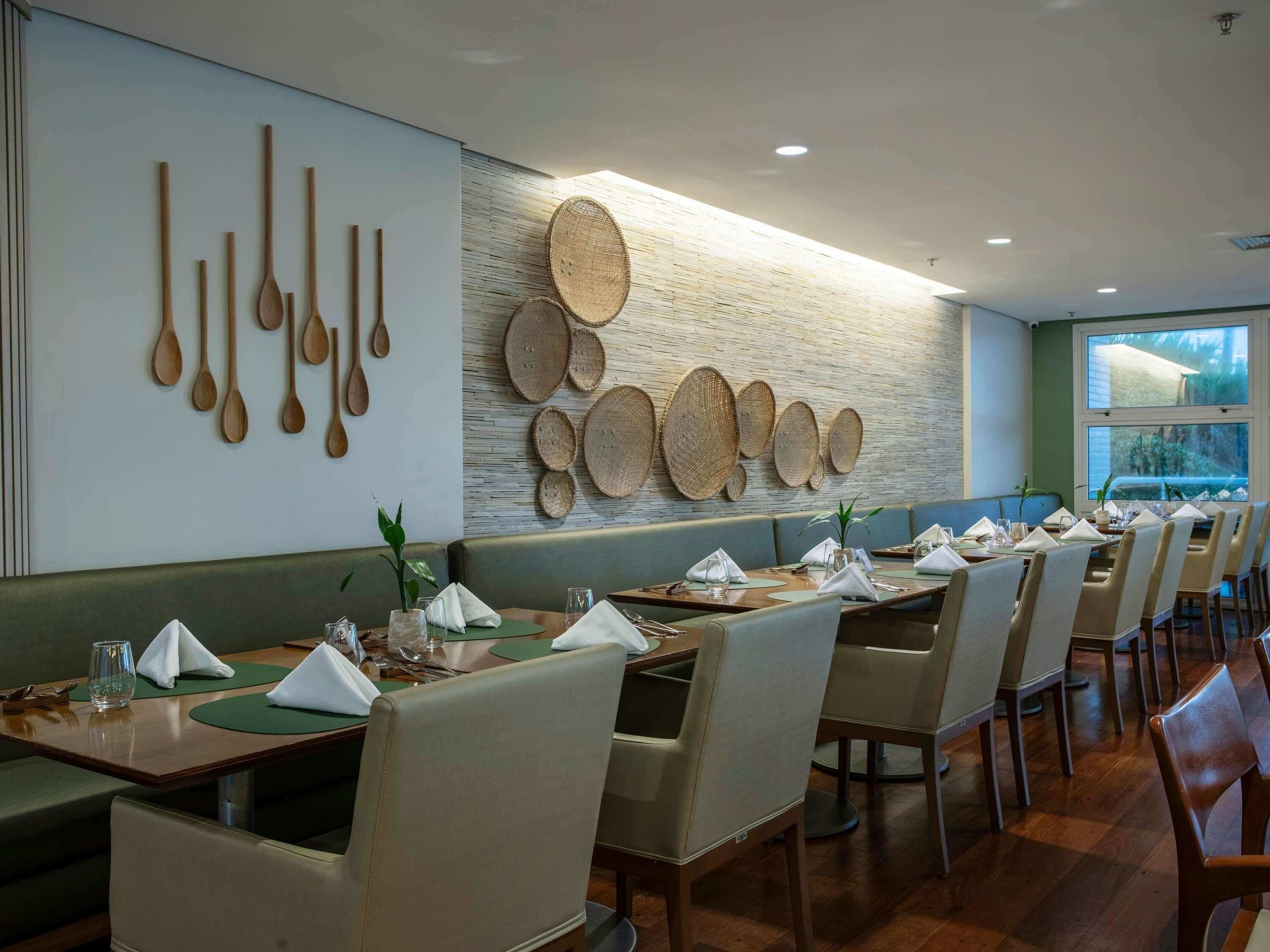 Ein Restaurant mit langen Gemeinschaftstischen, gepolsterten Sitzecken und einer Wand, die mit Holzlöffeln und gewebten Körben verziert ist.